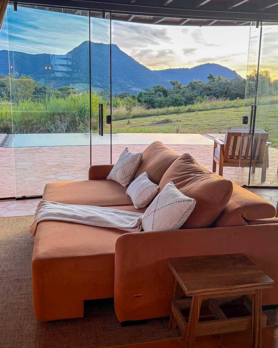 El living abierto de par en par al atardecer: el sofá, la mesa y, del otro lado del vidrio, la piscina y el Cerro Amor.