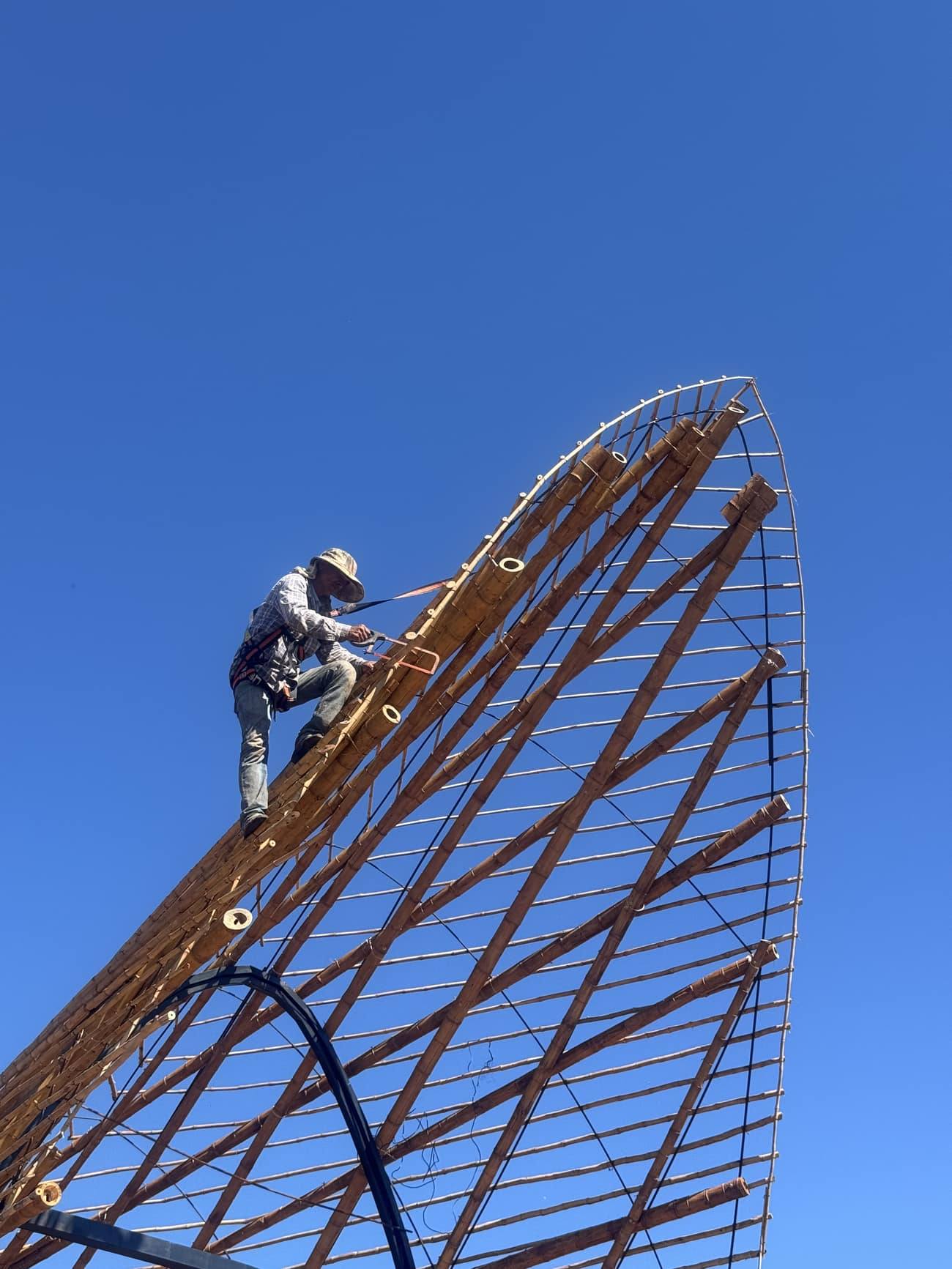 Un obrero en lo alto de la estructura, atando la tacuara contra el cielo.